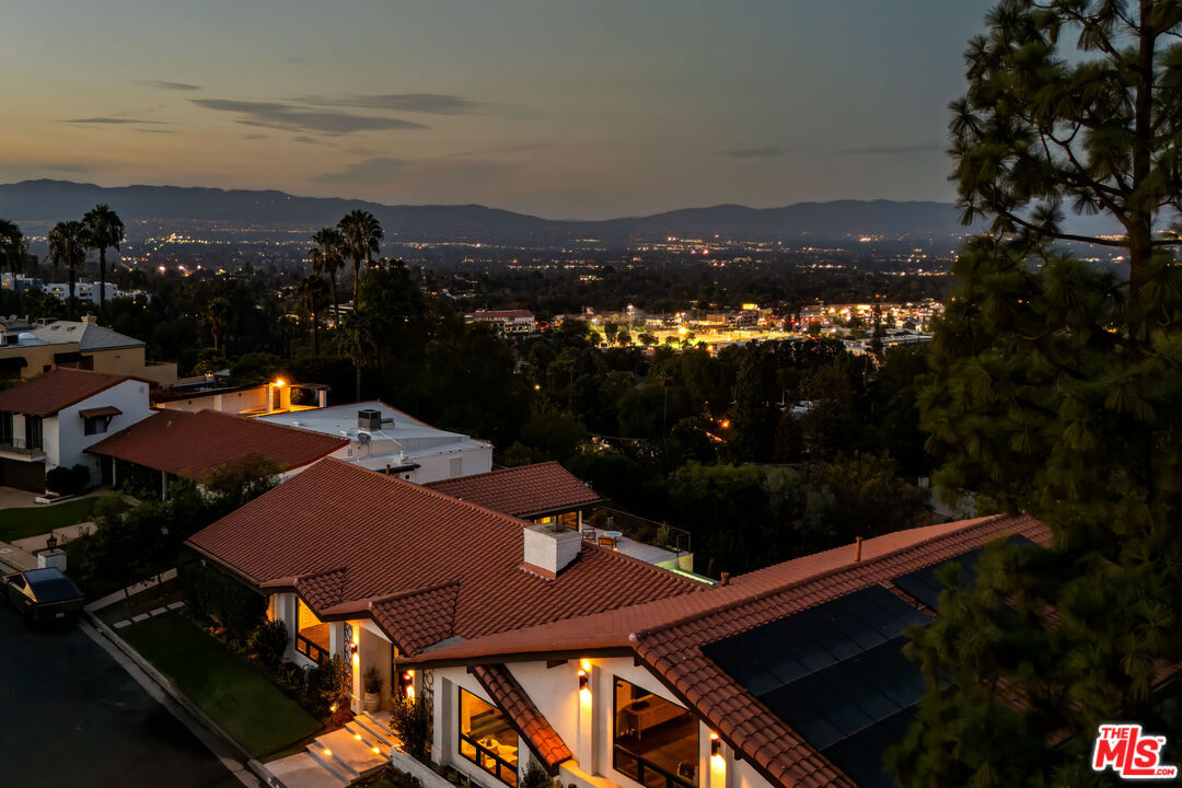 Aerial twilight view of the property's tiled roofline, solar array, and the lit San Fernando Valley below