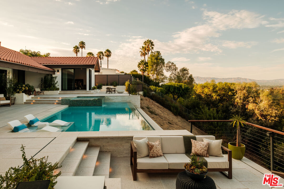 Wide dusk view of the pool, spa, and terrace along the length of the house