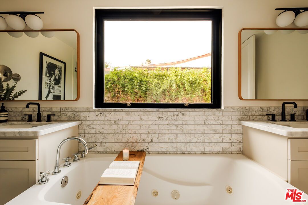 Primary bathroom with facing marble vanities and a window-lit soaking tub