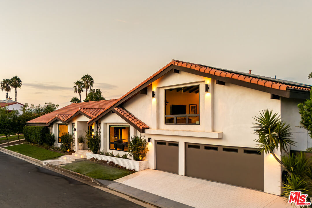 Twilight view of the tiled-roof mid-century home with warm interior lighting and mature palm trees
